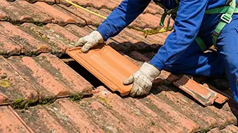 Substituição de telha de cerâmica quebrada realizada por profissional com equipamento de segurança em altura